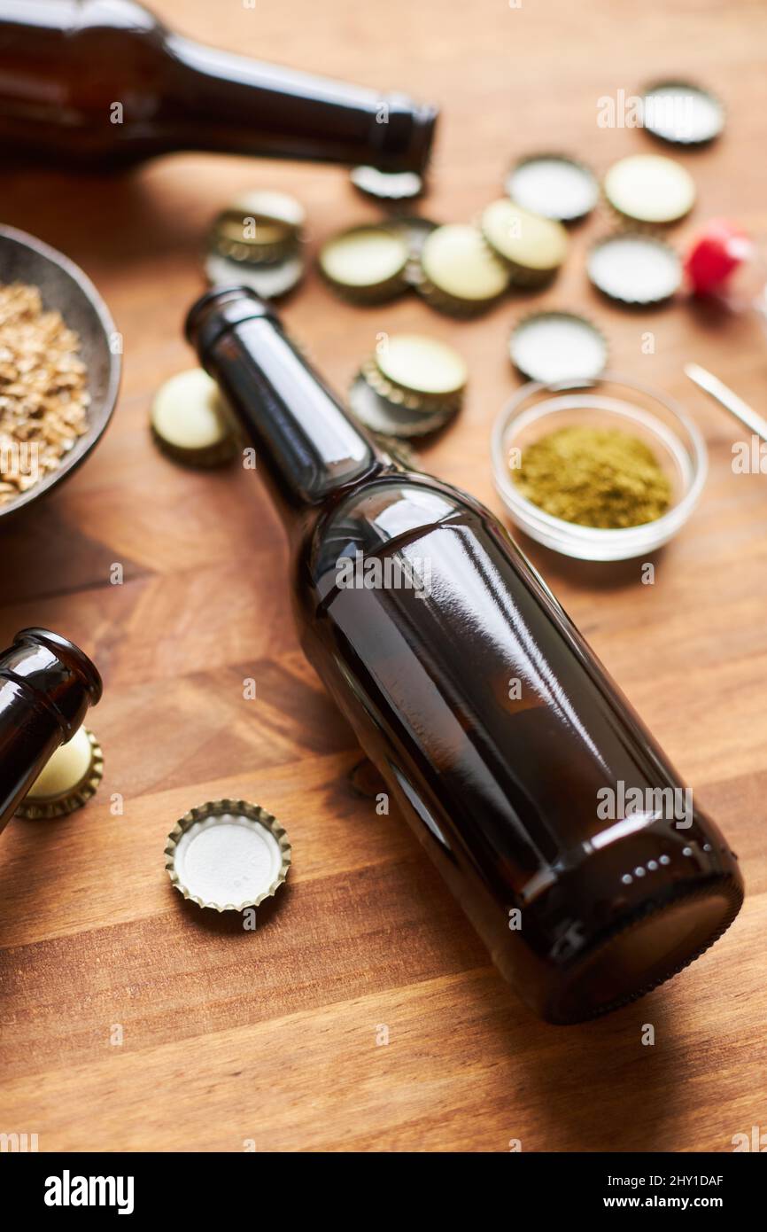 Glasflasche in der Nähe einer Schüssel mit Gerstenkörnern und Metallkappen auf dem Tisch mit Thermometer für die Herstellung von hausgemachtem Bier Stockfoto