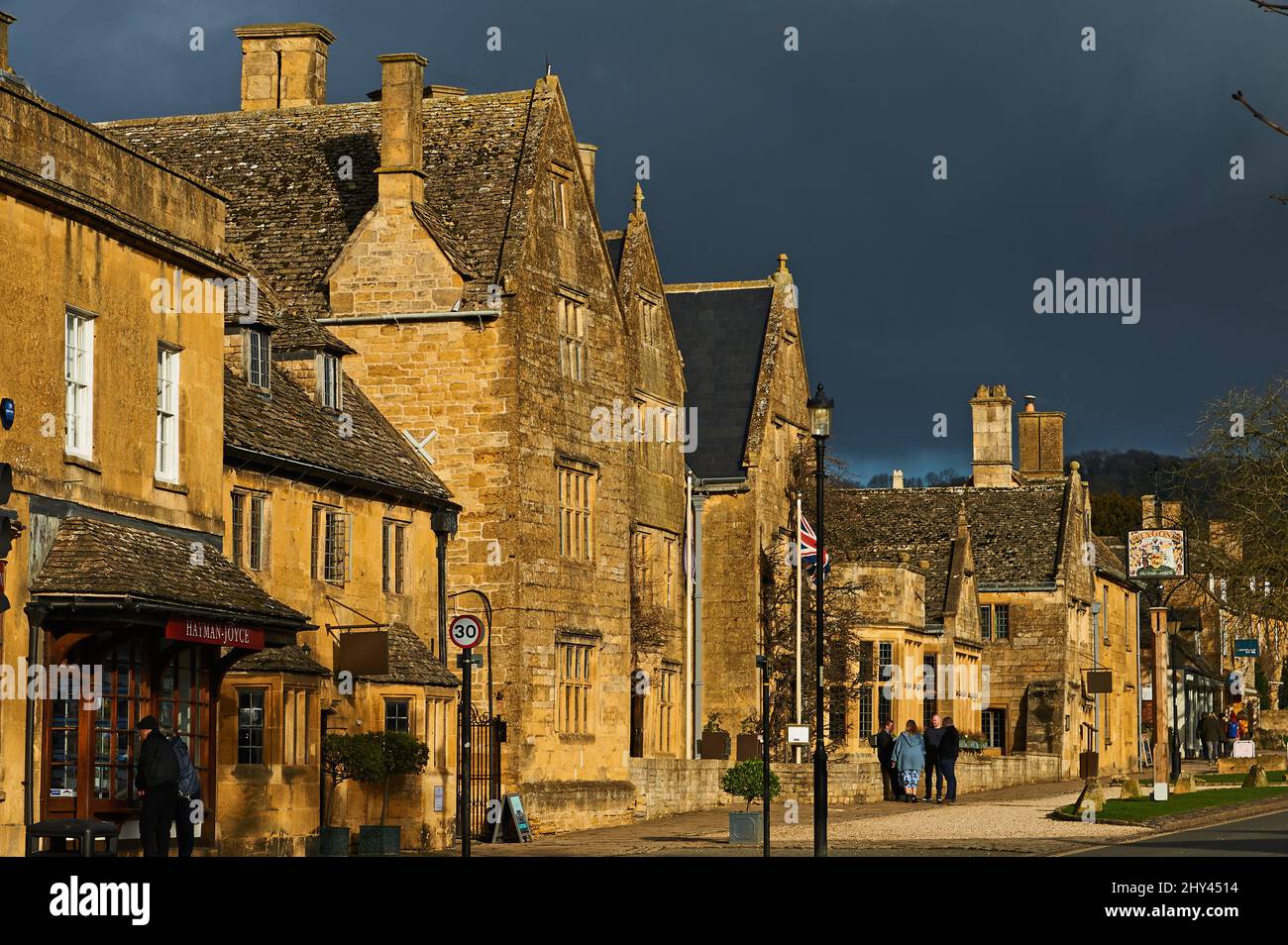 High Street Broadway in den Cotswolds mit Gebäuden, die unter einem stürmischen Himmel hervorgehoben werden Stockfoto