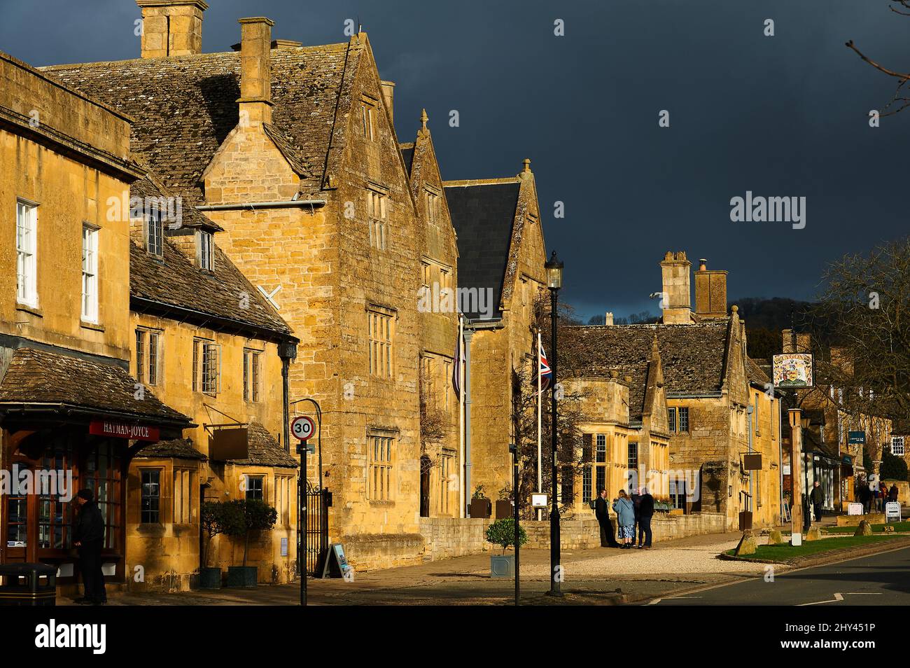 High Street Broadway in den Cotswolds mit Gebäuden, die unter einem stürmischen Himmel hervorgehoben werden Stockfoto