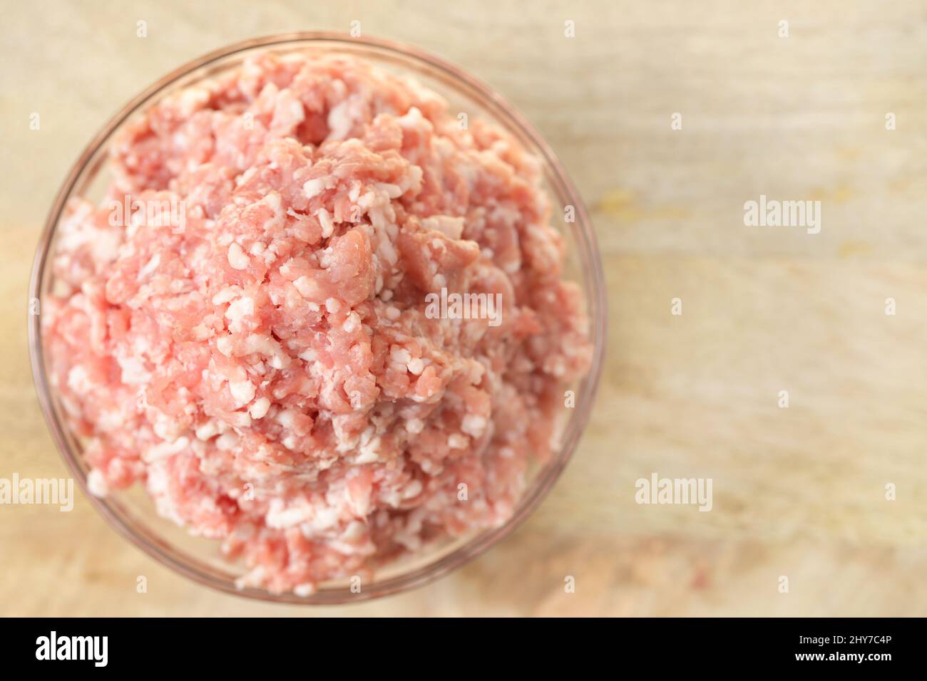 Hackfleisch aus Schweinefleisch. Frisches Hackfleisch aus nächster Nähe in einer transparenten Tasse auf einem Holztisch. Fleischprodukte.frisch gemahlenes Fleisch aus der Nähe Stockfoto