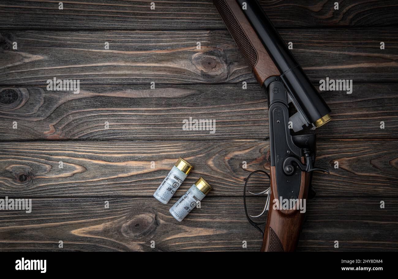 Auf einem Holztisch geöffnetes Doppelkarrell-Jagdgewehr. Schrotflinte-Ammo. Dunkelbrauner Holzhintergrund. Stockfoto