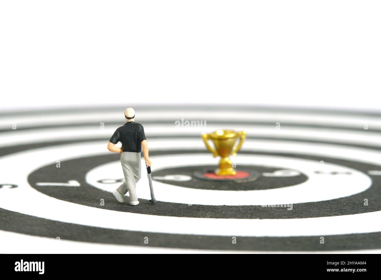 Miniatur Menschen Spielzeug Figur Fotografie. Ein Golfer für Männer, der über der Dartscheibe steht, mit einer goldenen Trophäe in der Mitte, isoliert auf weißem Hintergrund. Bild pho Stockfoto