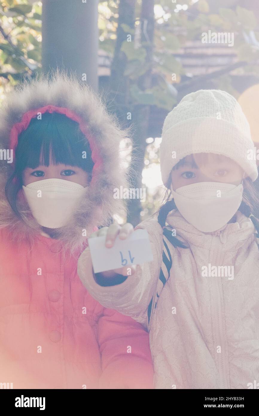 Kinder in schützender Gesichtsmaske und Winterkleidung sitzen und warten, um sich mit der Familie auf das Wandern in der Natur vorzubereiten. Aktivitäten lernen und na erkunden Stockfoto