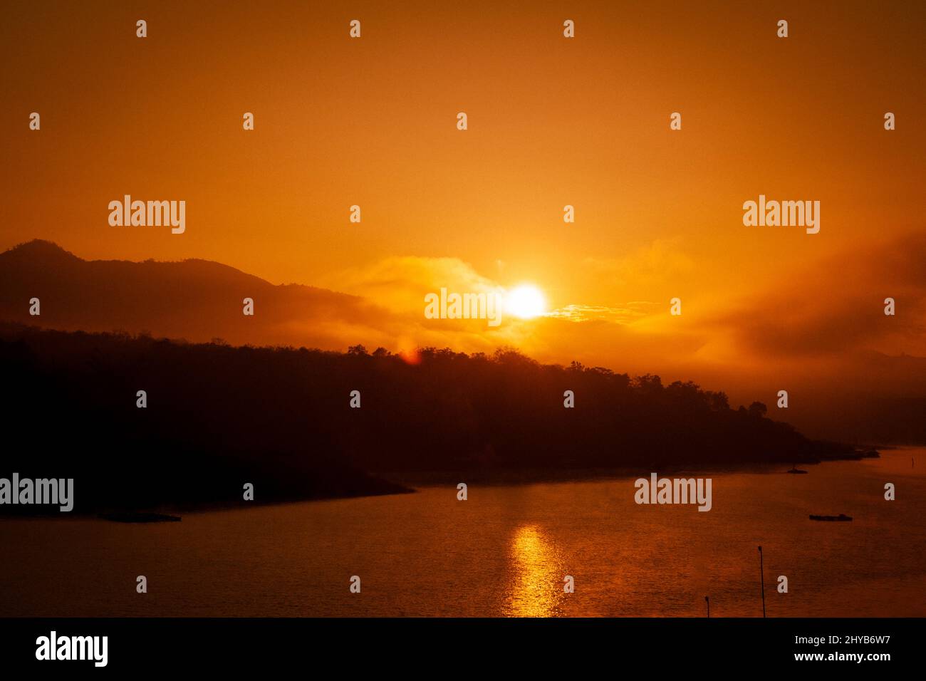 Schöner Sonnenaufgang über dem See mit warmem Himmel und funkelnden Reflexen auf der Wasseroberfläche. Stockfoto