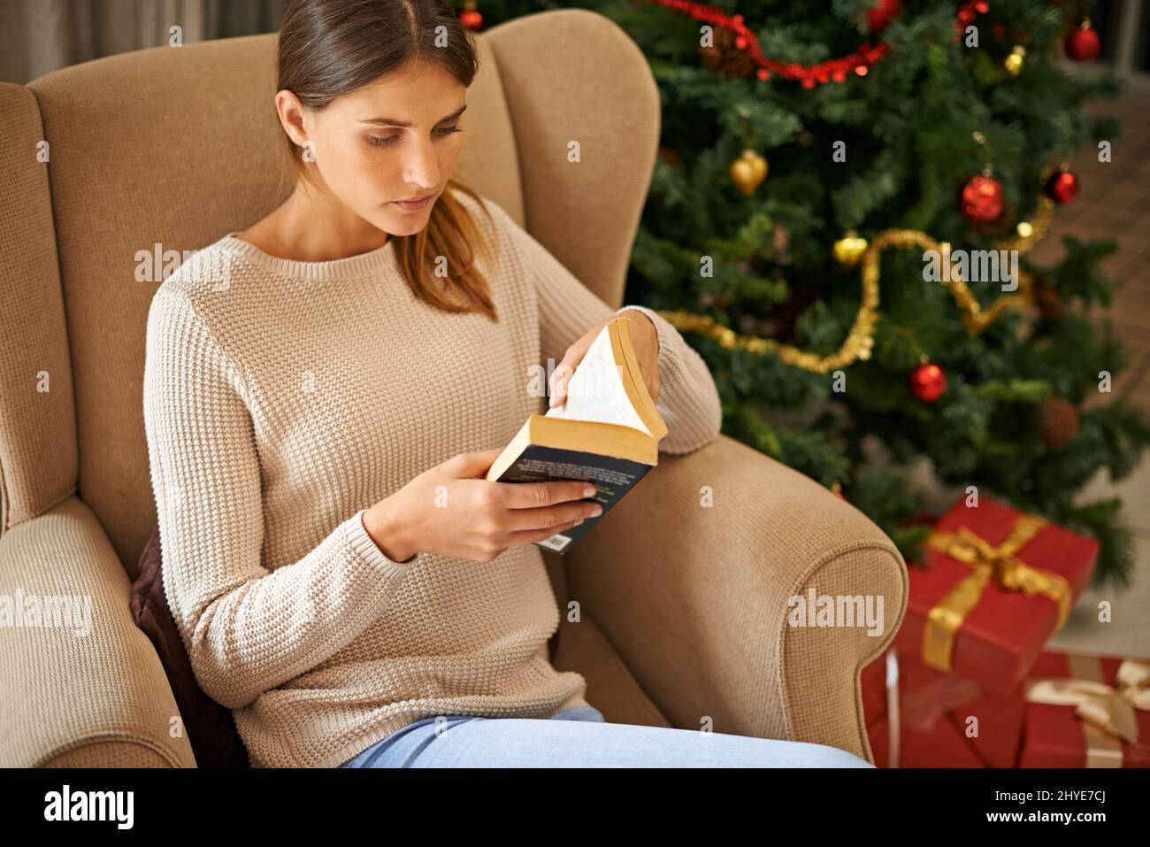 Ich kann kein gutes Buch preisgeben. Aufnahme einer schönen jungen Frau, die während der Weihnachtsferien zu Hause ein Buch liest. Stockfoto