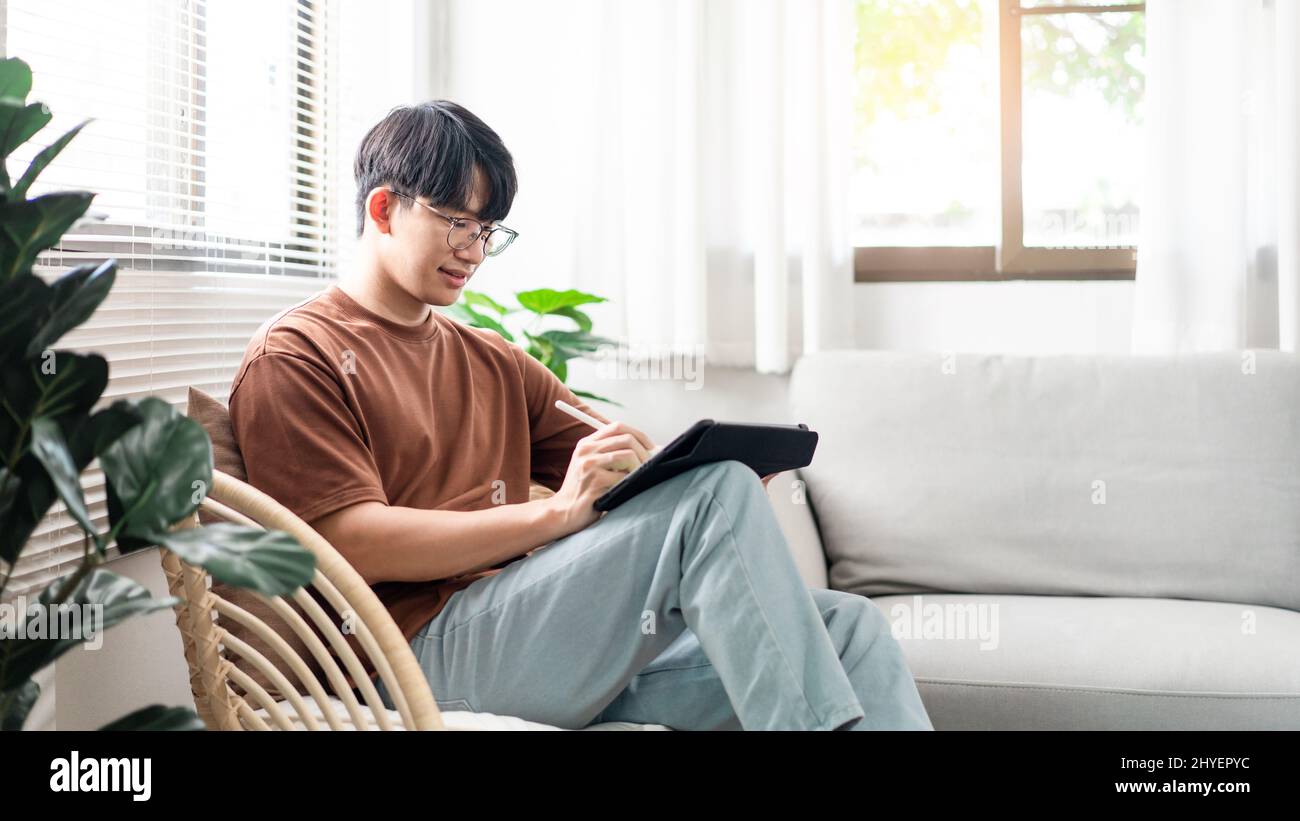 Technologiekonzept der Mann mit seinem lässigen T-Shirt und Jeans sitzt bequem auf dem Holzstuhl und macht einen Touchscreen, um die Webbrowsen zu überprüfen Stockfoto