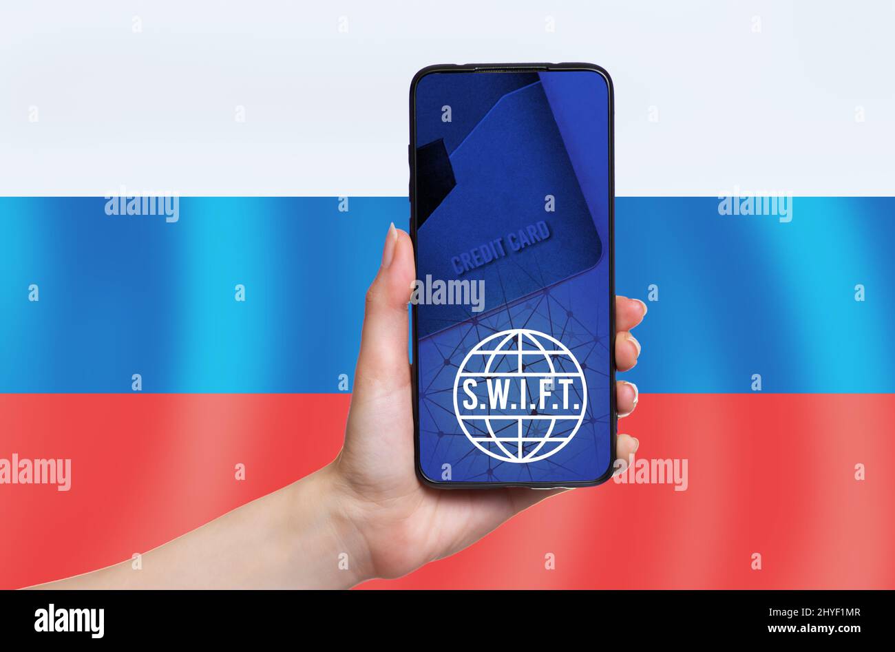 Die Hand einer Frau hält ein Mobiltelefon. Auf dem Smartphone-Bildschirm Zeichen von S.W.I.F.T. Speicherplatz kopieren. Die russische Flagge ist im Hintergrund. Das Konzept von i Stockfoto