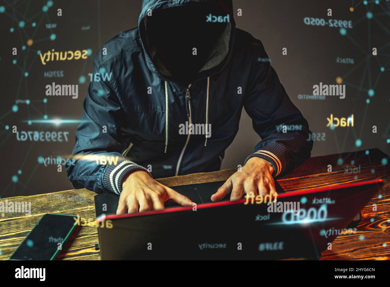 Ein anonymer Hacker in einer Haube tippt auf einer Laptop-Tastatur in einem dunklen Raum. Das Konzept der Cyber-Kriegsführung und Dos-Angriffe Stockfoto