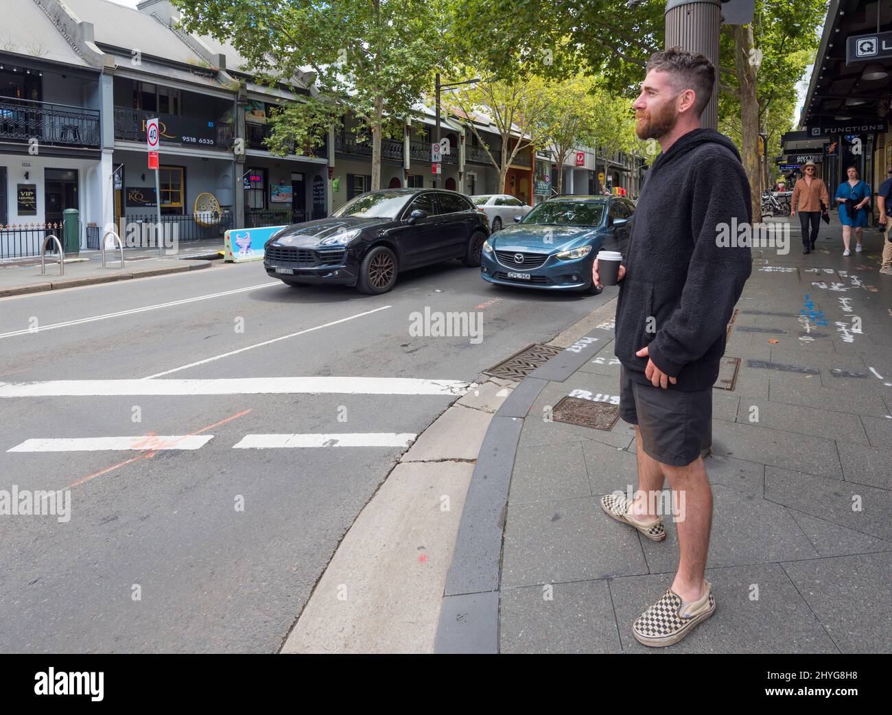 Ein junger Australier mit Bart, Shorts und Pullover steht an einer Ampel, die in Ultimo, Sydney, Australien, zu überqueren wartet Stockfoto