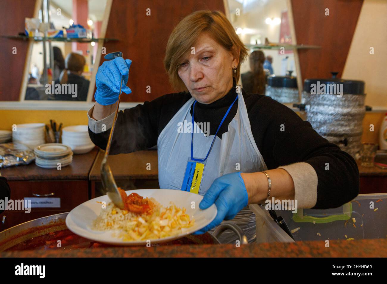 USCHHOROD, UKRAINE - 14. MÄRZ 2022 - Ein Freiwilliger legt in einem Restaurant, das Binnenvertriebenen kostenlose Mahlzeiten anbietet, Essen auf den Teller Stockfoto