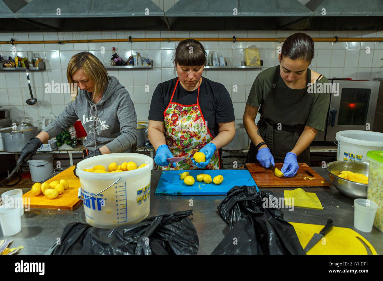 USCHHOROD, UKRAINE - 14. MÄRZ 2022 - drei Freiwillige schneiden Kartoffeln in einem Restaurant, das Binnenvertriebenen kostenlose Mahlzeiten anbietet Stockfoto
