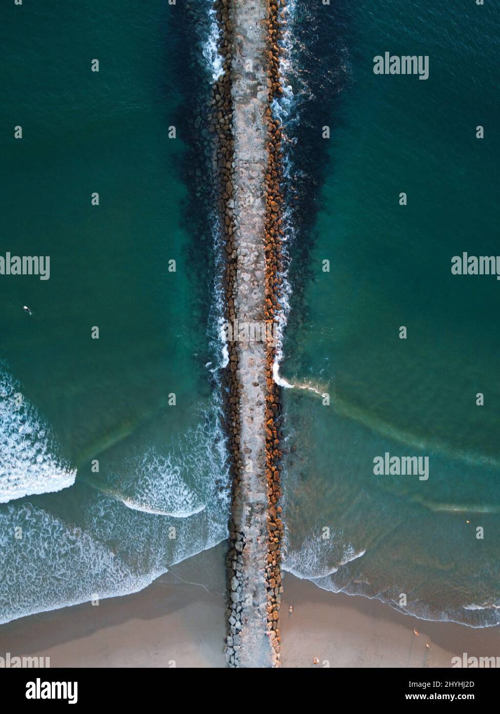 Luftaufnahme von Meereswellen, die auf Felsen um einen Steinwharf krachen, der das Meer in zwei Hälften teilt Stockfoto