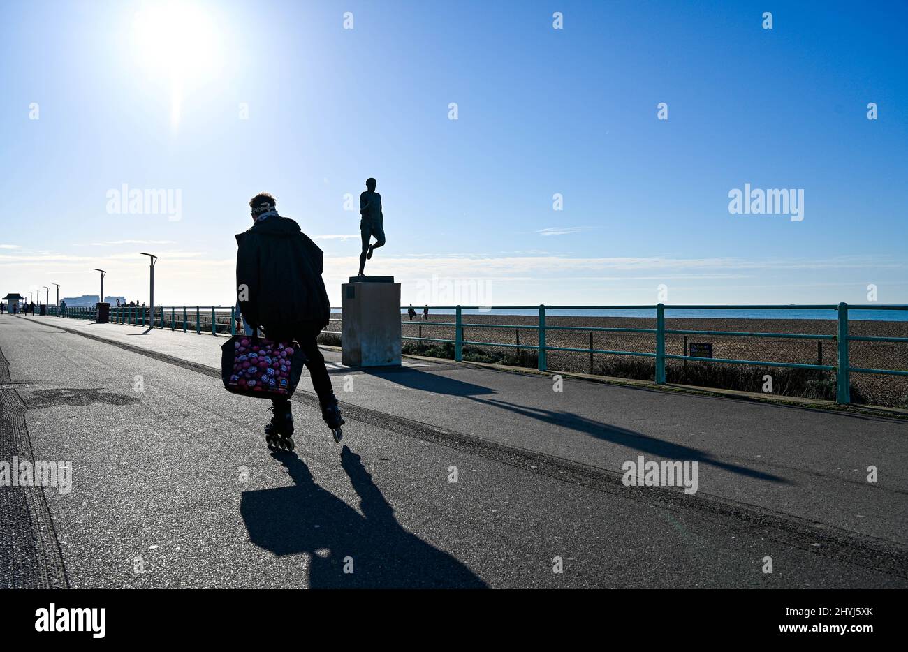 Brighton UK 7. March 2022 - Ein Rollerblader kommt an der Steve Ovett Statue an der Strandpromenade von Brighton vorbei an einem schönen sonnigen Tag, an dem sich das Wetter in den nächsten Tagen über Großbritannien ausbreiten wird : Credit Simon Dack / Alamy Live News Stockfoto