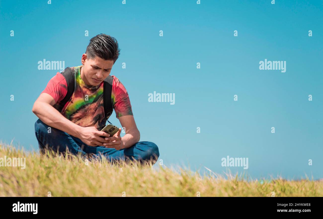 Backpacker mit Telefon auf einem Hügel, ein Mann, der mit seinem Handy auf dem Gras sitzt Stockfoto