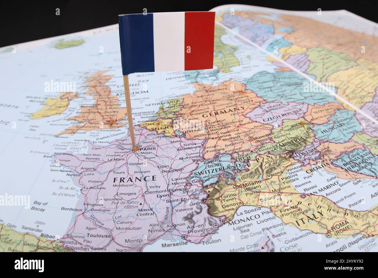 Die Nationalflagge Frankreichs stopfte in eine farbige Landkarte des französischen Landes. Ein offener Atlas, der Lage und Text von Paris und den Nachbarländern zeigt Stockfoto