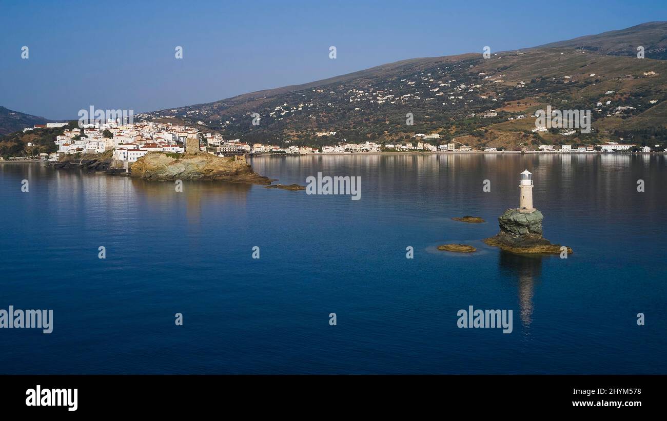 Drohnenaufnahme, niedrige Höhe, Blick auf weißen runden Leuchtturm auf winzigen felsigen Insel und Altstadt von Chora, Häuser auf Landzunge, hügelige Landschaft in Stockfoto