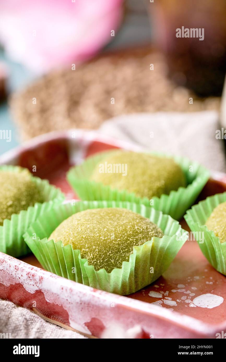 Nahaufnahme von asiatischen traditionellen Reis Dessert süßen grünen Matcha-Mochi in rosa Keramik-Gericht auf blauem Tisch. Frühling rosa Blumen im Hintergrund. Stockfoto