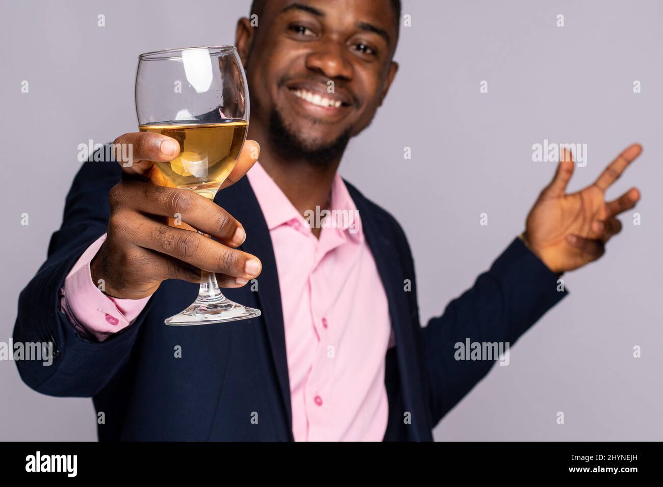 Aufgeregt junger schwarzer Mann, der ein Glas Wein auf einem hellvioletten Hintergrund aufwirft Stockfoto