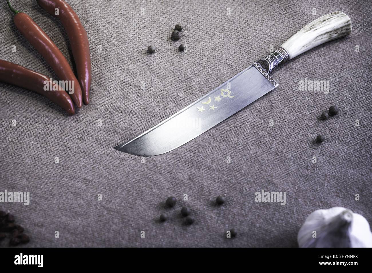 Draufsicht auf ein scharfes, dekoratives Messer, umgeben von Pfeffer und Knoblauch auf einer öffentlichen Fläche Stockfoto