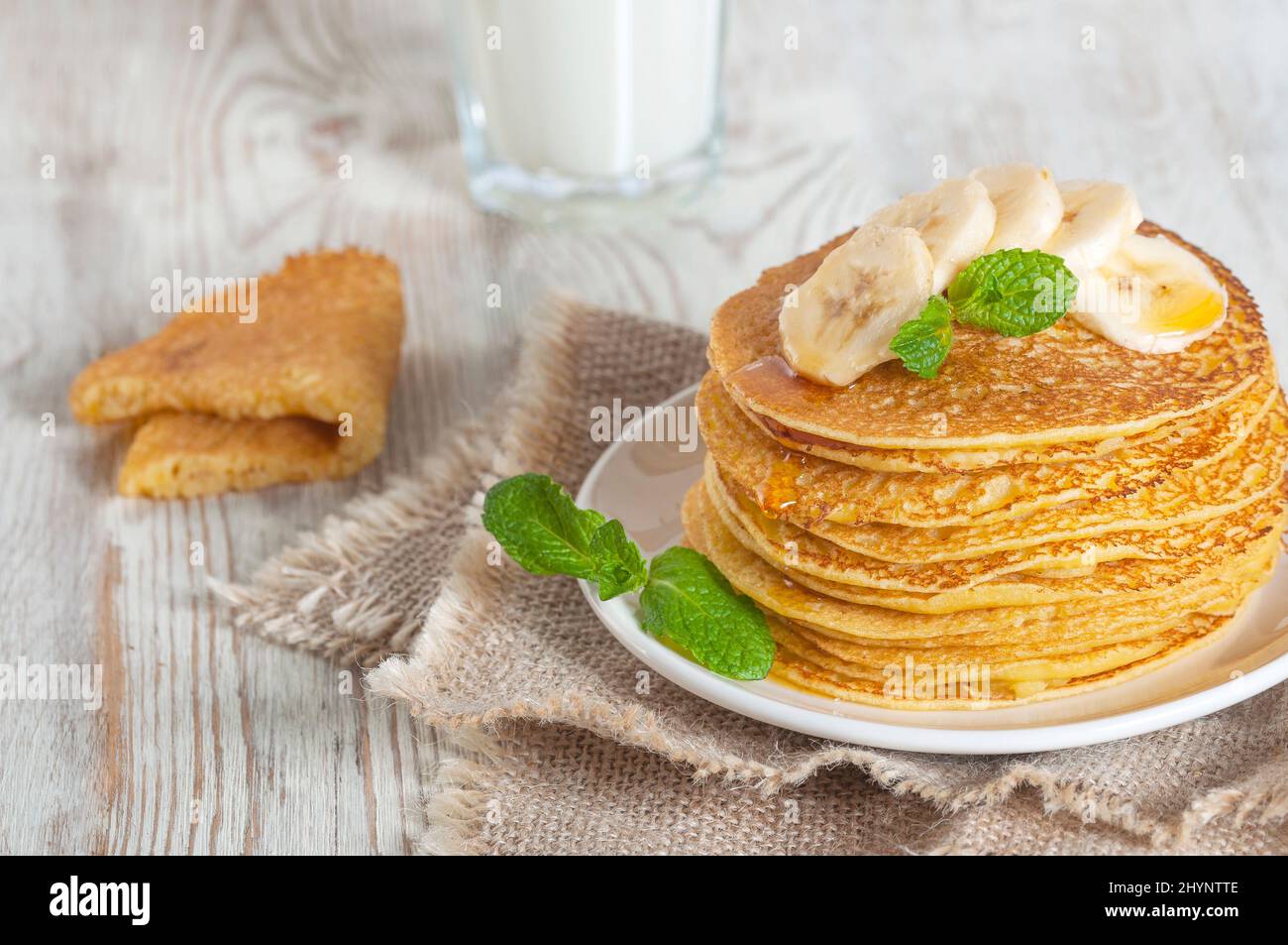 Pfannkuchen mit Milch serviert, garniert mit Minzblättern und Bananenscheiben. Mit Honig oder Ahornsirup gegossen. Stockfoto