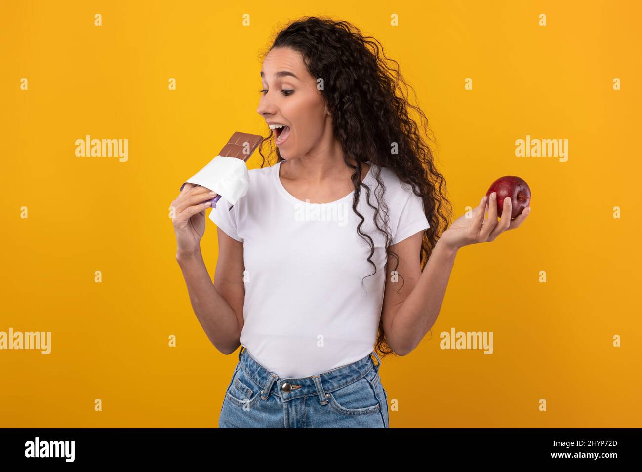 Porträt einer aufgeregten Dame, die Apfel hält und Schokolade beißt Stockfoto