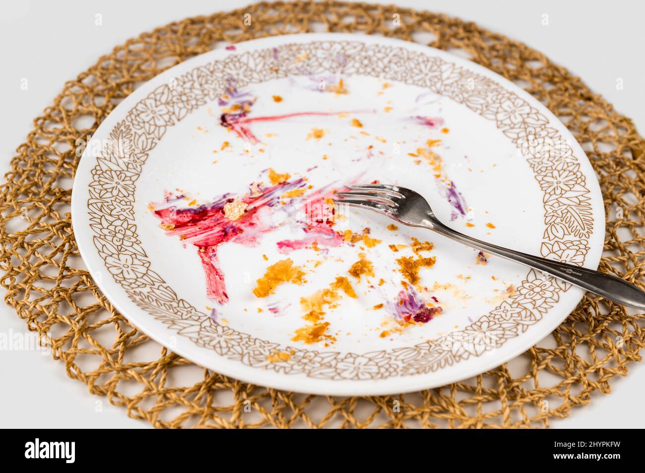 Schmutziger leerer Teller mit Krümel aus Blätterteig und buntem Fruchtfleisch, Gabel, Bambuskissen auf weißem Hintergrund. Stockfoto