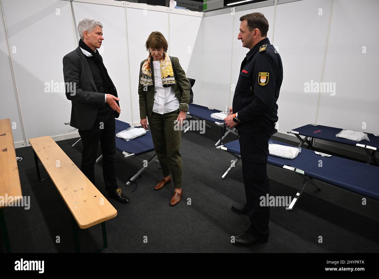 Köln, Deutschland. 15. März 2022. Harald Rau (l.), Leiter des Referats V - Soziales, Gesundheit und Wohnen der Stadt Köln, Henriette Reker, Oberbürgermeisterin der Stadt, und Christian Miller, Leiter der Berufsfeuerwehr, stehen in einer Schlafzelle in einer Ausstellungshalle. Die Stadt bietet bis zu 1.100 Schlafplätze in der Halle für ukrainische Flüchtlinge. Quelle: Federico Gambarini/dpa/Alamy Live News Stockfoto