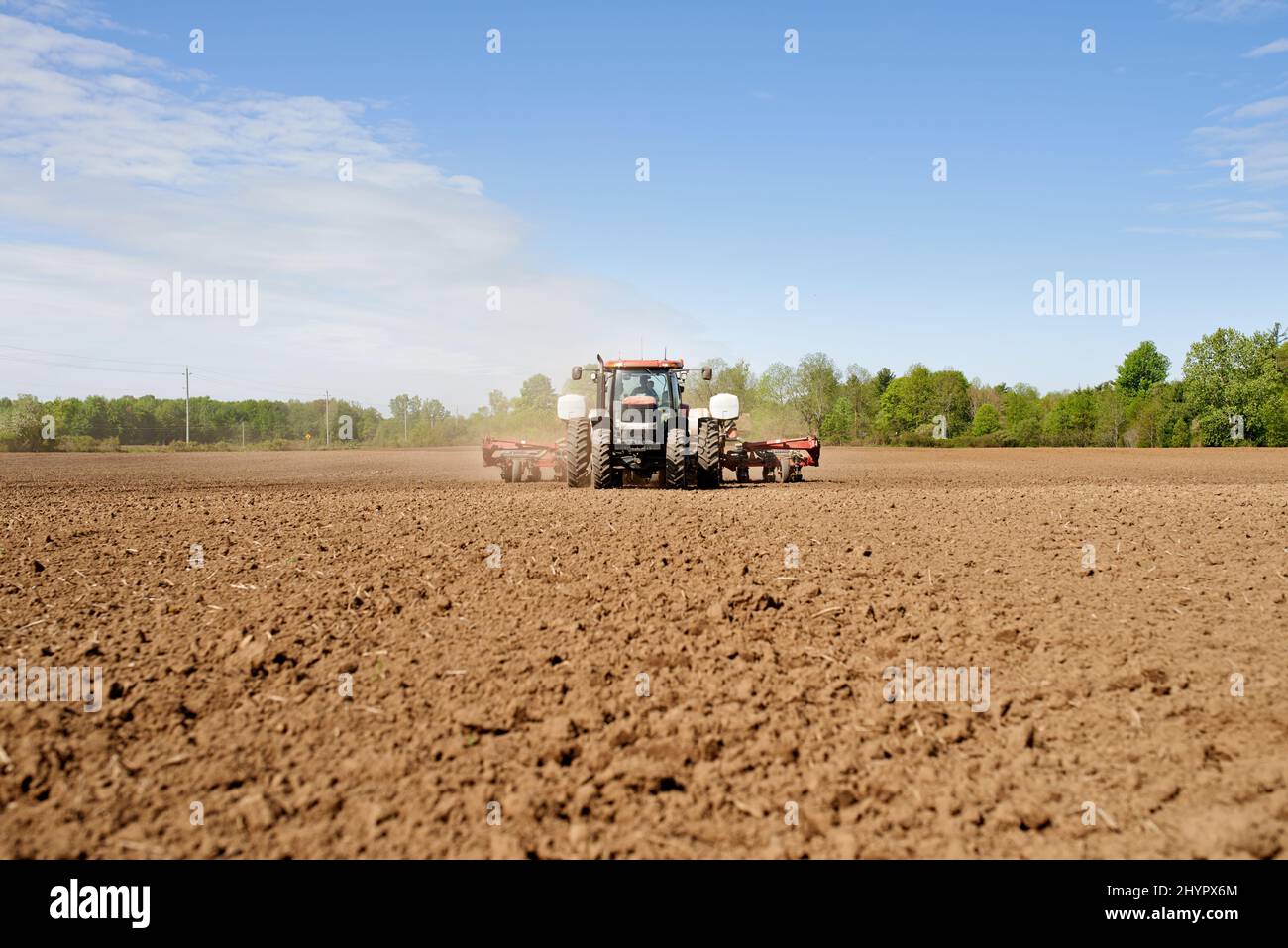 Das Land säen. Aufnahme eines Traktors, der ein großes gepflügeltes Feld auf einem Bauernhof sät. Stockfoto