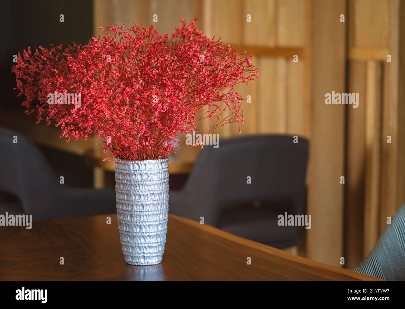 Schöne silberne Vase mit Sandstruktur und roter Pflanze in einem Holztisch, auf dem sich der Arbeitsplatz in einem Gebäude teilt, leerer Raum für Text. Stockfoto