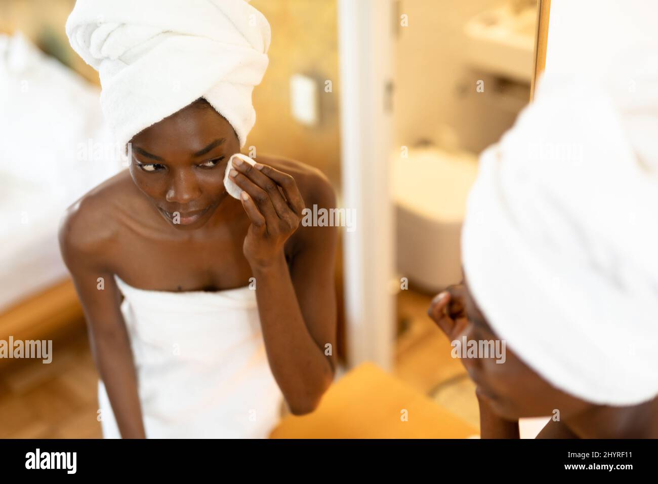 afroamerikanische Frau, die Schwamm Wange reiben, während sie Spiegelreflexion im Badezimmer betrachtet Stockfoto