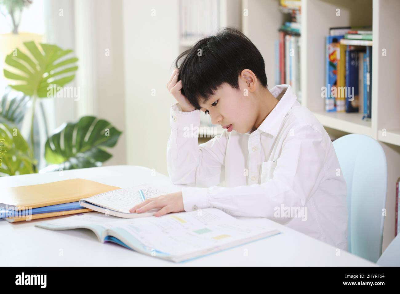 Ein Kind, das genug von den aufgetürmten Schulaufgaben und dem langwierigen Studium hat, lernt, indem es schwierige Probleme mit einem müden Blick löst. Stockfoto