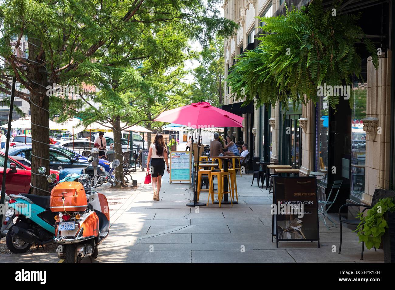ASHEVILLE, NC, USA-22 JULY 2021: Ein Sommertag auf Page Ave. In der Innenstadt, der Menschen an Straßencafé-Tischen zeigt, eine gut gekleidete Frau, die vorbeigeht. Stockfoto