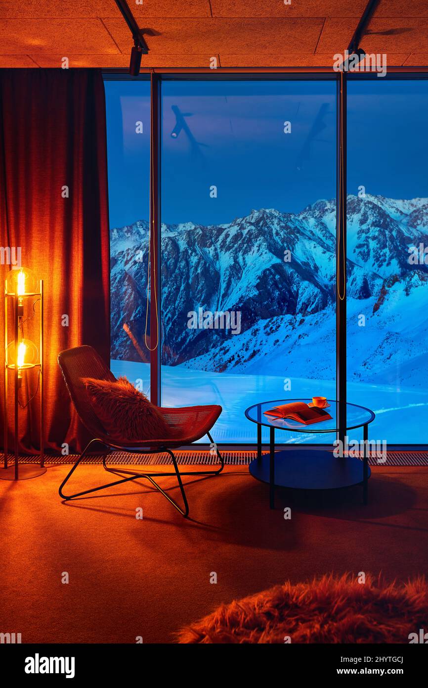 Loft Interieur mit Stuhl und Tisch im Zimmer in der Nähe Panoramafenster mit blauen Berg und glühen orange Lampe im Hotel in Shymbulak Skigebiet Almaty, Stockfoto