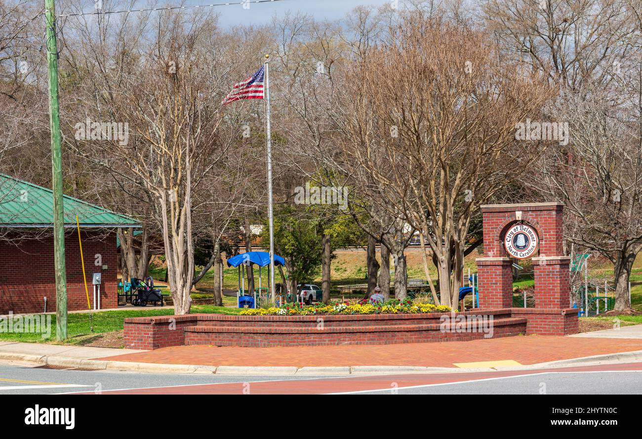 BELMONT, NC, USA-8. MÄRZ 2022: Ecke des Stowe Park, mit Blumenbeet und Denkmalschild für 'City of Belmont'. Ein Mann sitzt hinter Blumenbeet. Stockfoto