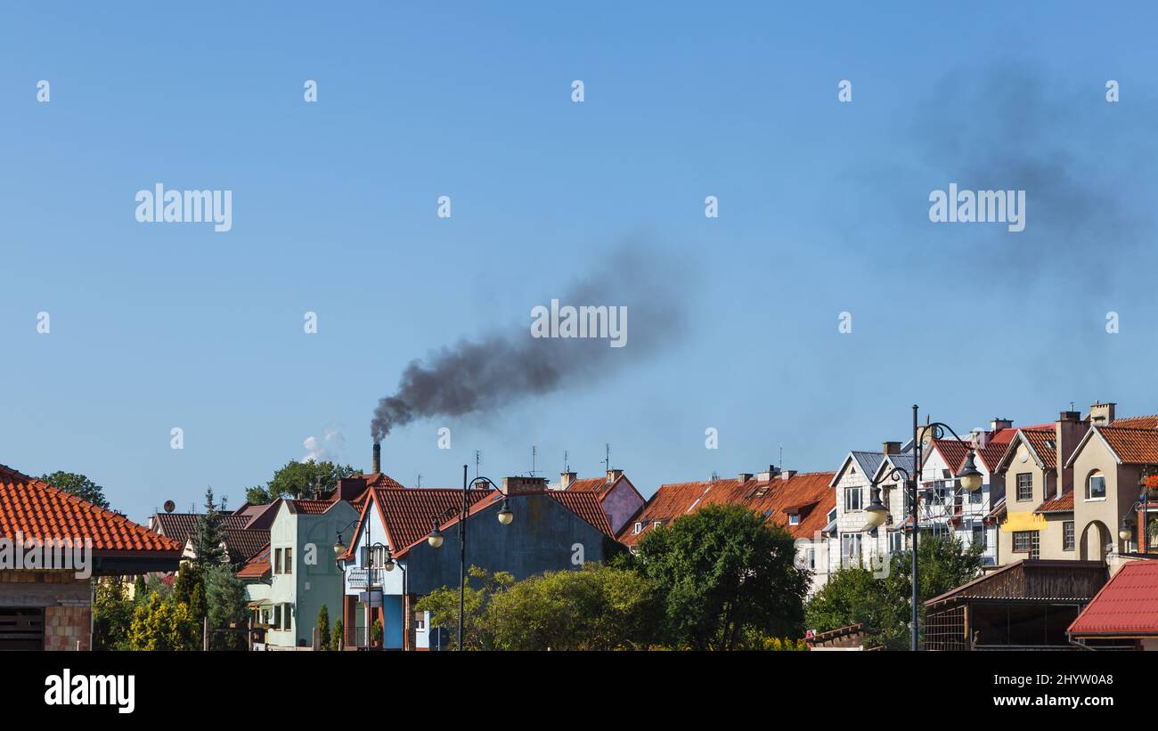 Luftverschmutzung, schwarzer Rauch aus dem Kamin über dem Stadtgebiet, kleine Einfamilienhäuser in der Stadt gegen blauen Himmel mit Kopierraum Stockfoto