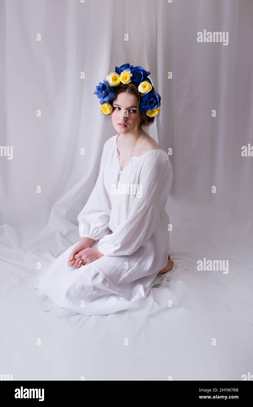 Schöne ukrainische Frau in einem weißen Kleid und Blumenkranz auf weißem Hintergrund. Symbol der ukrainischen gelb-blauen Flagge. Die ruhige Dame. Frieden in der Ukraine Stockfoto