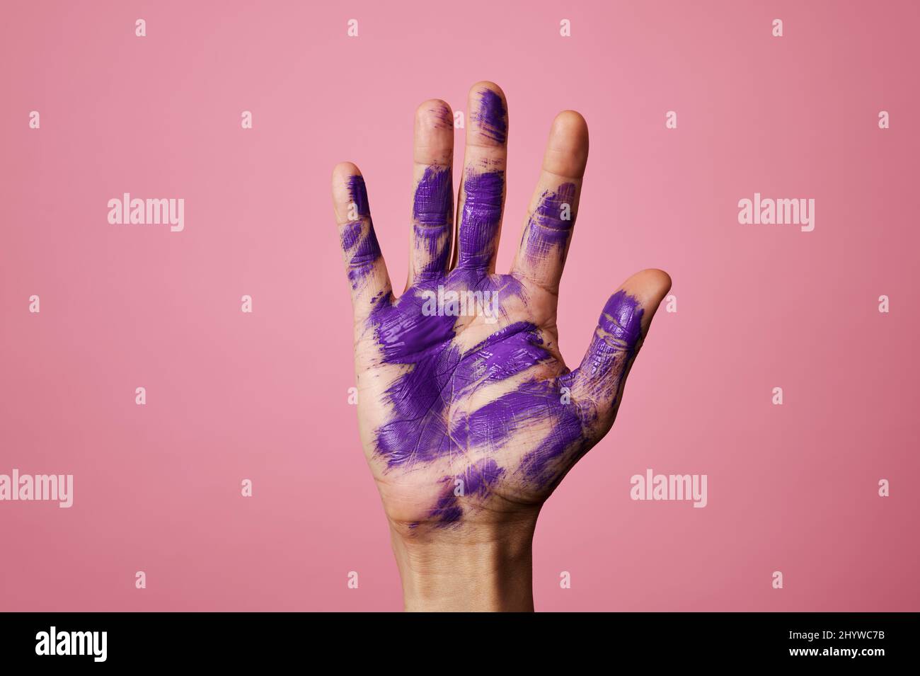 Nahaufnahme der erhobenen Hand eines Mannes mit einigen Flecken lila Farbe, auf einem rosa Hintergrund Stockfoto