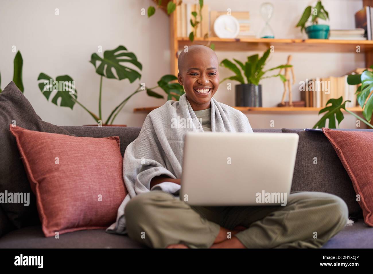 Eine junge Frau sitzt mit ihrem Laptop auf der Couch und lächelt Stockfoto