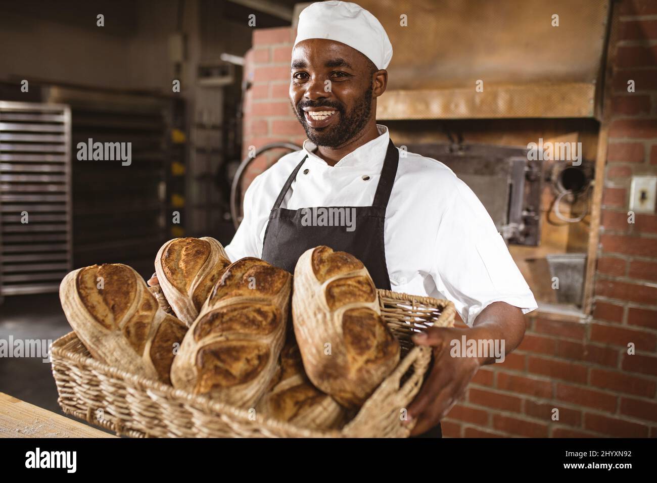 Porträt eines lächelnden afroamerikanischen Bäckerers mit mittlerem Erwachsenen, der einen Weidenkorb mit Brot hält Stockfoto