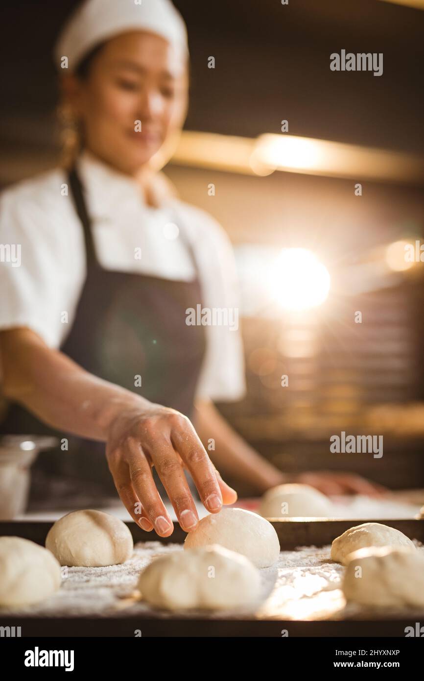 Asiatische Mitte Erwachsene weibliche Bäcker Kommissionierung Teigkugel während der Herstellung von Brot in der Bäckerei Stockfoto