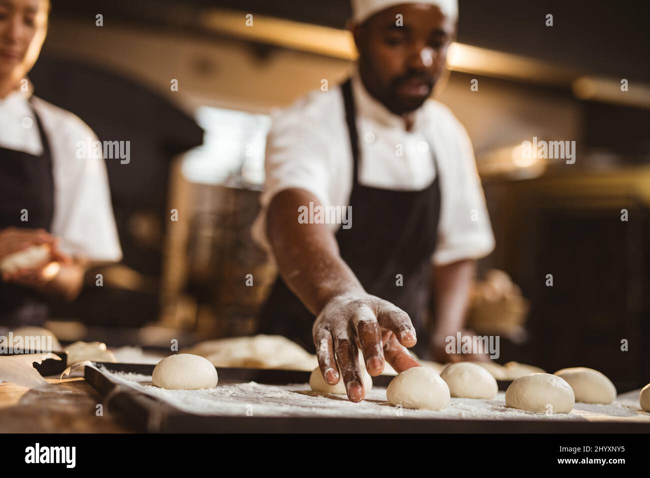 afroamerikanischer mittelerwachsener männlicher Bäcker pflücken Teigkugel, während er Brot in der Bäckerei macht Stockfoto