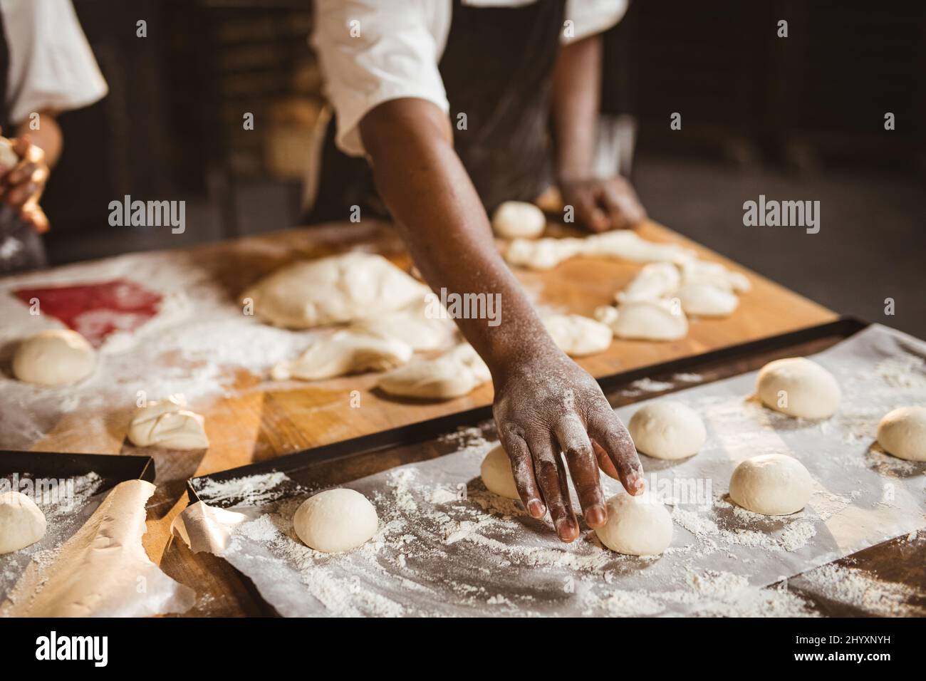 Mittelteil des afroamerikanischen mittelerwachsenen männlichen Bäckers, der beim Brotbacken eine Teigkugel pflückte Stockfoto