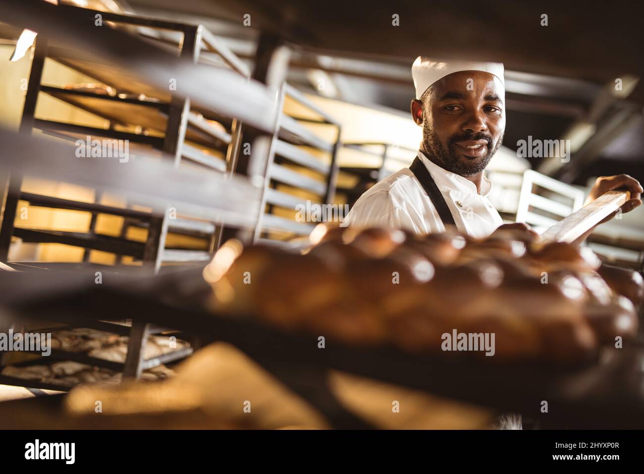 afroamerikanischer Bäcker mit mittlerem Erwachsenen, der geflochtene Brottablett im Regal hält Stockfoto