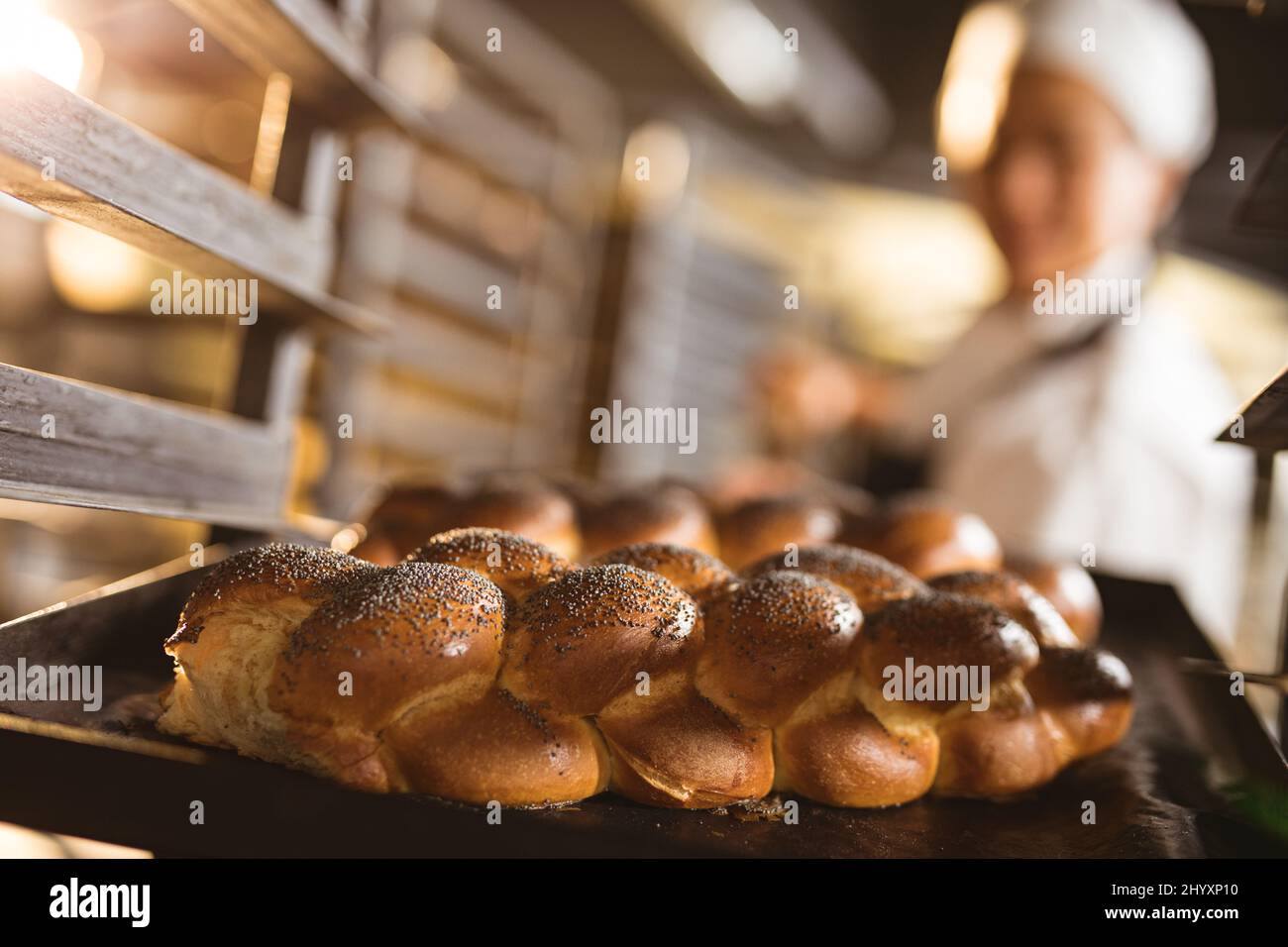 Asiatische mittlere Erwachsene weibliche Bäcker halten gebackene geflochtene Brot Tablett in Rack Stockfoto