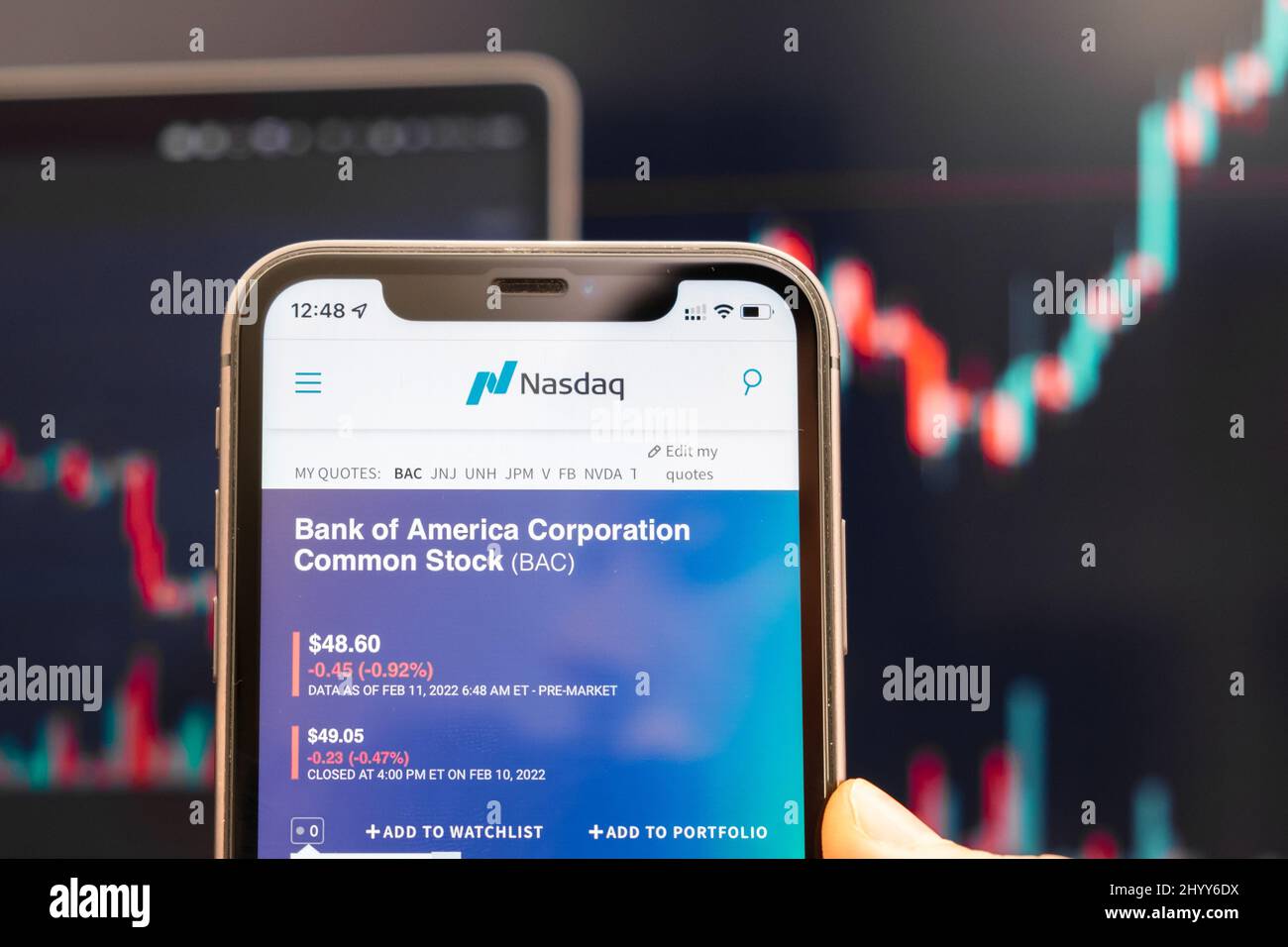 Bank of America Corporation Logo des Aktienkurses auf dem Bildschirm des Smartphones in mans Hand mit sich ändernden Trend auf dem Chart auf dem Hintergrund, Februar 2022, San Francisco, USA. Stockfoto