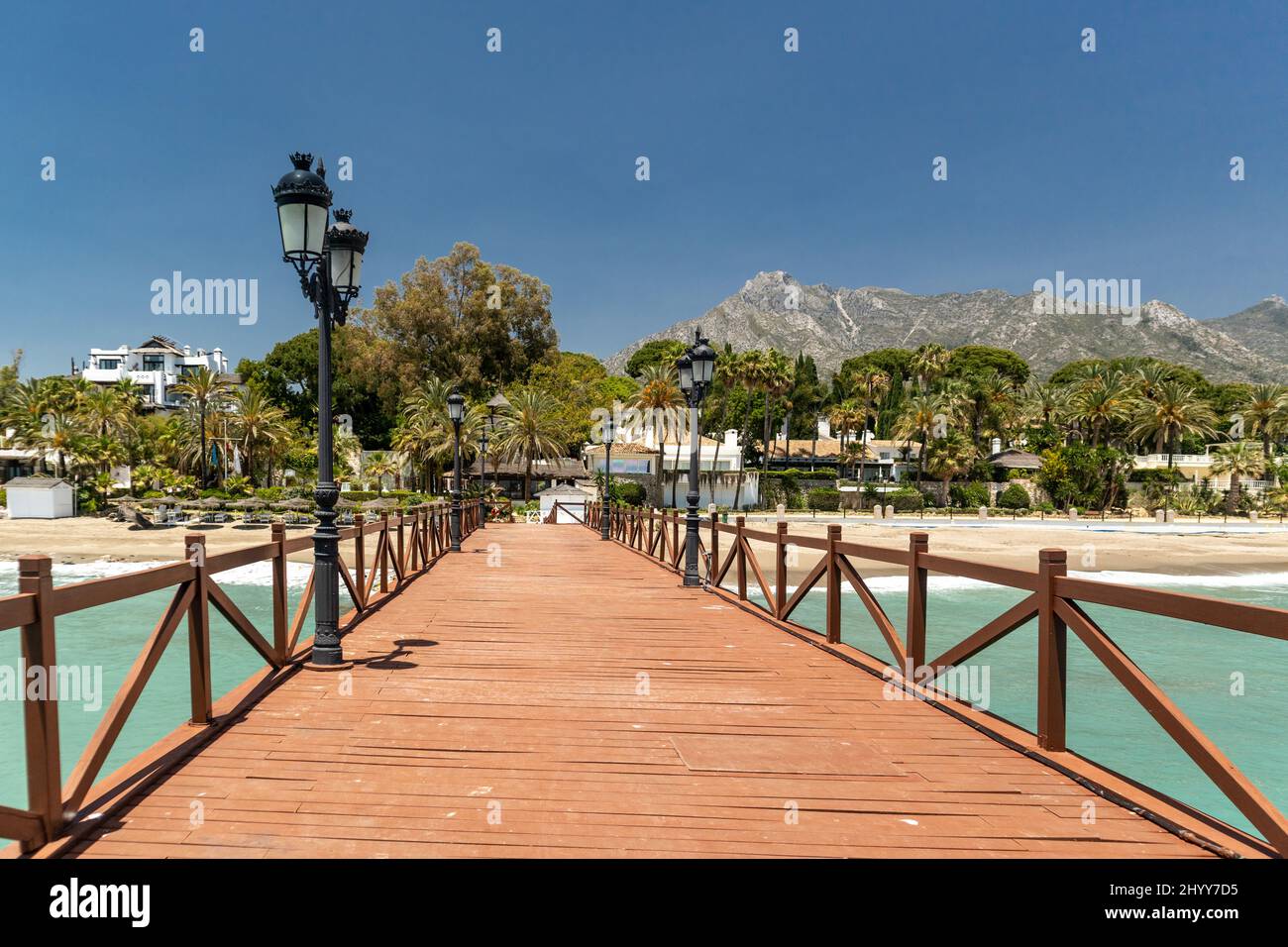 Blick auf die rote Holzbrücke 'Embarcadero' in Marbella. Blick auf das Luxusgebiet Puente Romano, teure Urbanisationen. Berg „La Concha“. Stockfoto