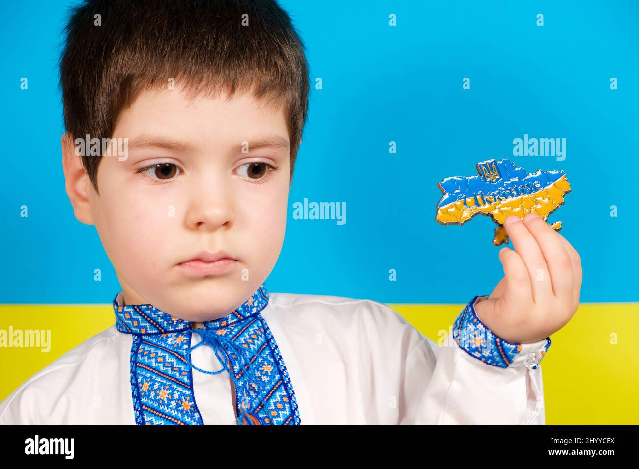 Ein trauriges ukrainisches Kind in Nationalkleidung hält eine Karte der Ukraine in der Hand. Krieg in der Ukraine Stockfoto