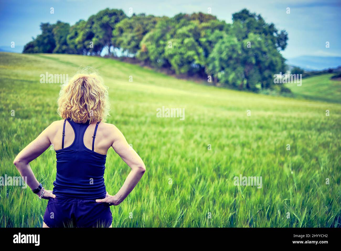 Back Portrait einer jungen reifen kaukasischen fit Frau mit blonden Haaren in Sportswear Outdoor in einer Getreidefarmlandschaft. Navarra, Spanien, Europa. Stockfoto