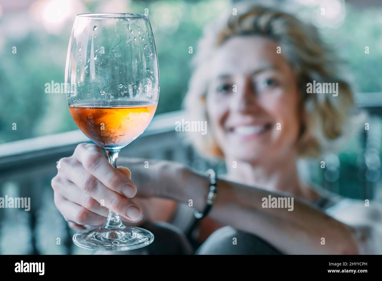 Porträt einer reifen kaukasischen blonden jungen Frau in den Fünfzigern, die auf der Veranda eines Hauses ein Glas Wein genießt. Lifestyle-Konzept. Stockfoto