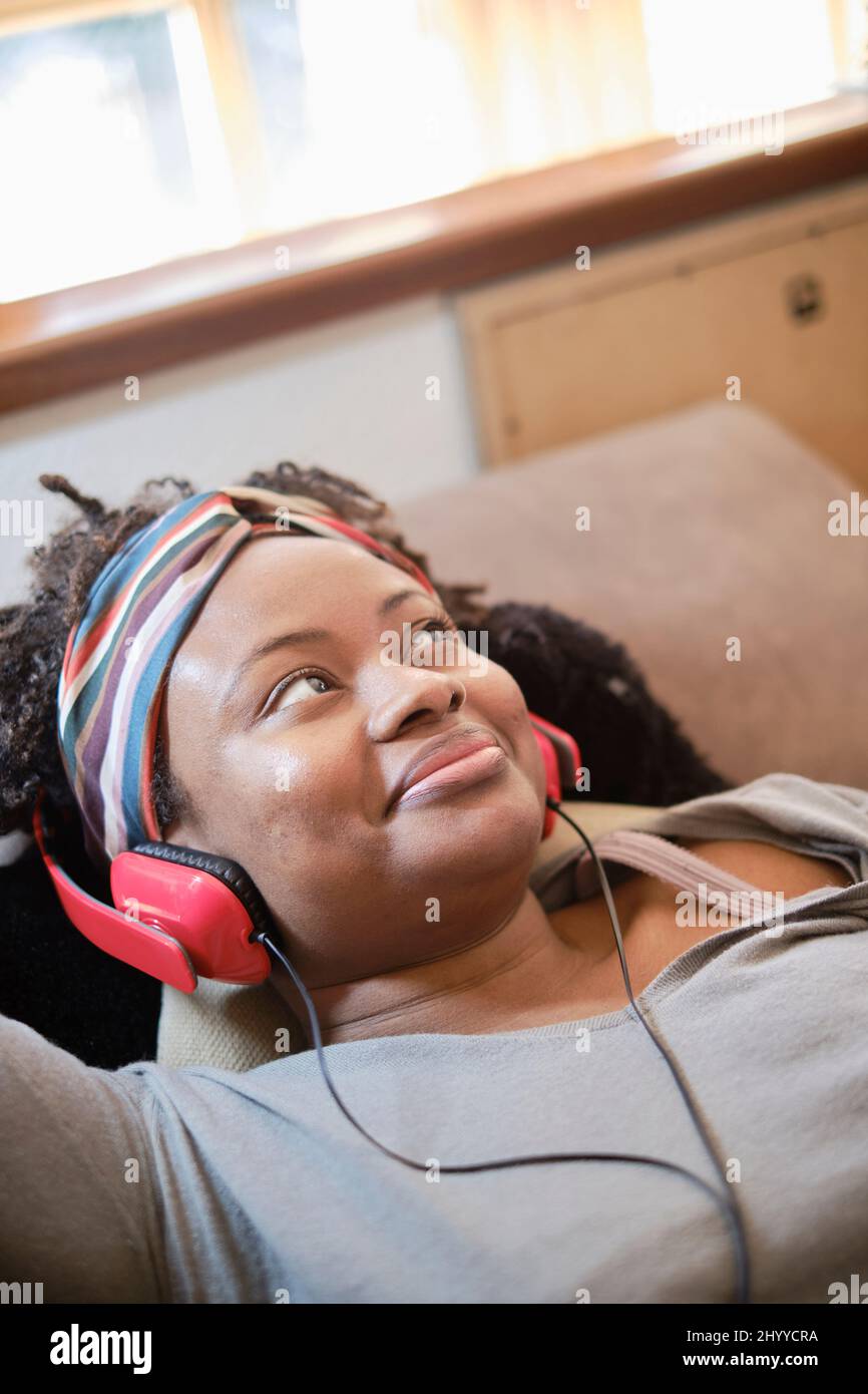 Porträt einer jungen schwarzen Frau, die mit Kopfhörern im Innenbereich Musik hört und auf einem Sofa liegt. Lifestyle-Konzept. Stockfoto